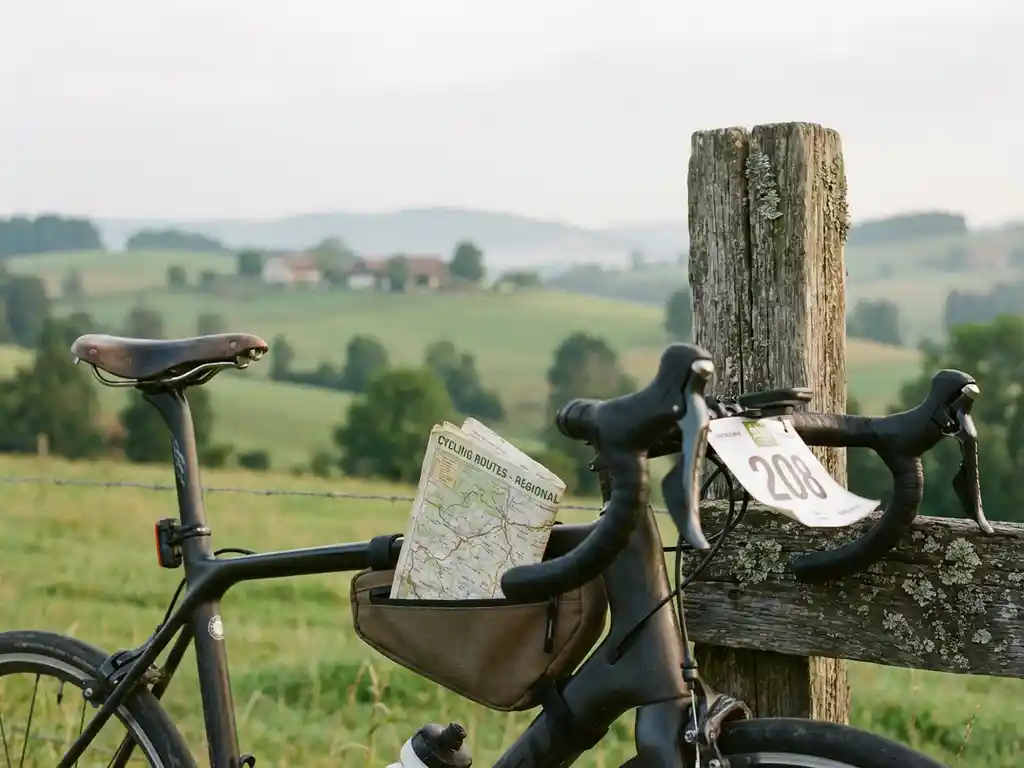Road bicycle with racing number leaning against wooden fence post with cycling map in frame bag, countryside hills in background