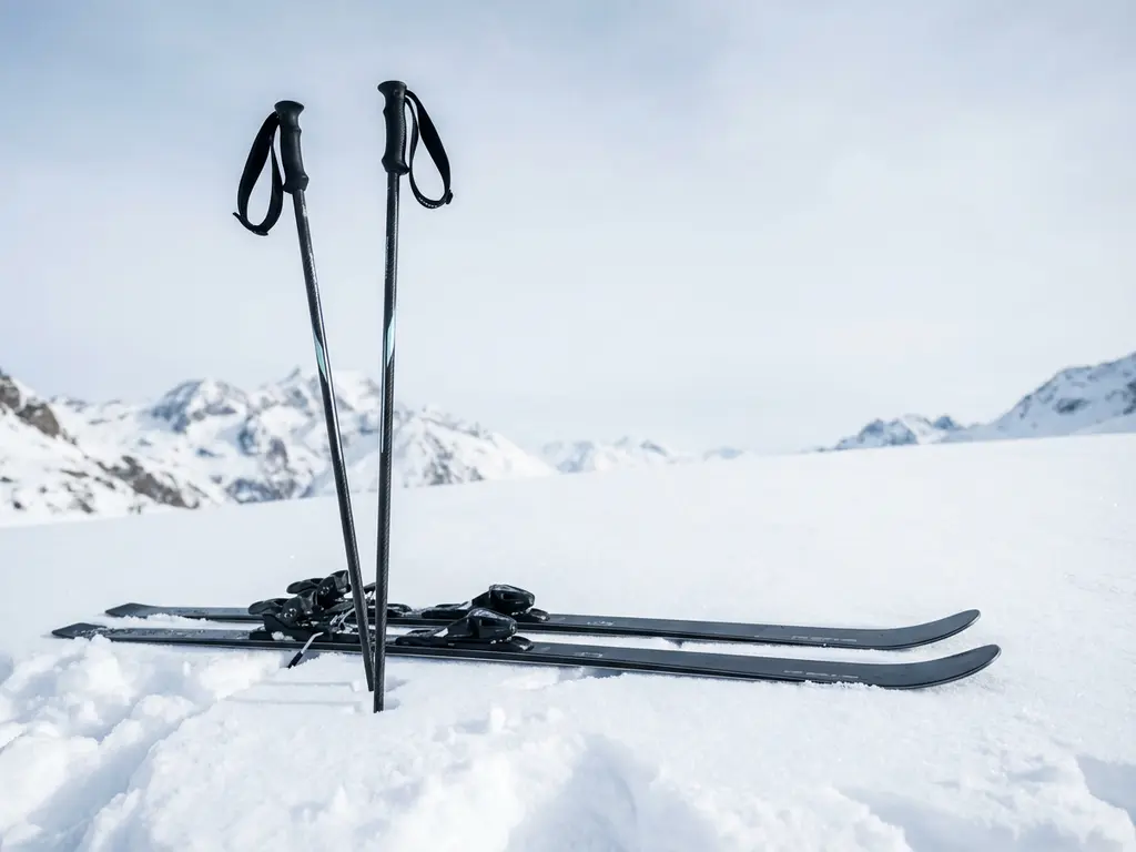 Black carbon fiber ski racing poles and skis in fresh powder snow with mountain peaks in background