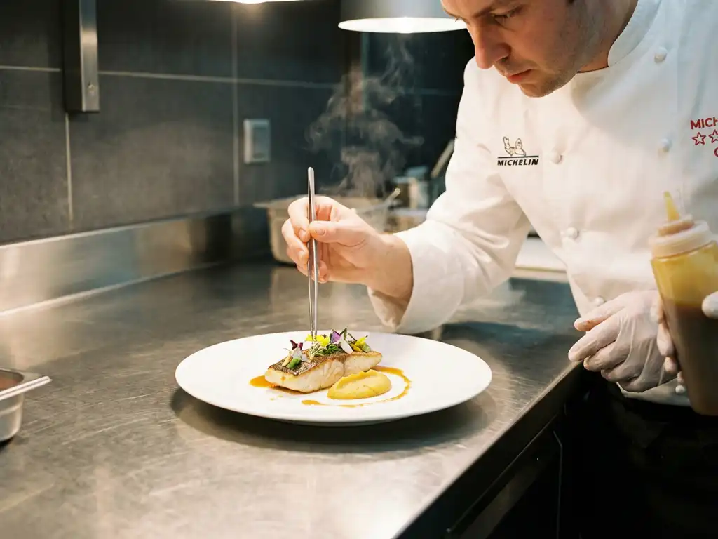Michelin-starred chef using tweezers to plate elegant dish with golden sauce drizzle on fine porcelain in professional kitchen